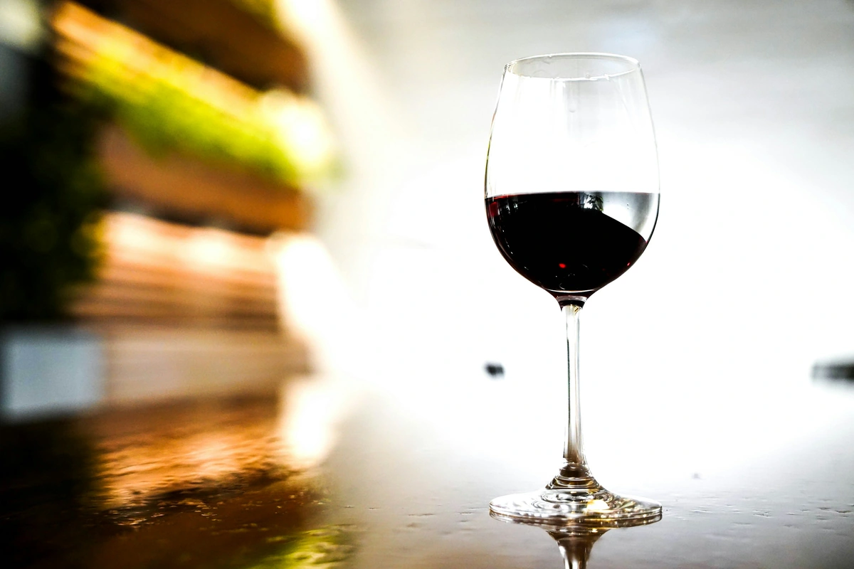 Taça de vinho tinto escuro sobre uma superfície de madeira.