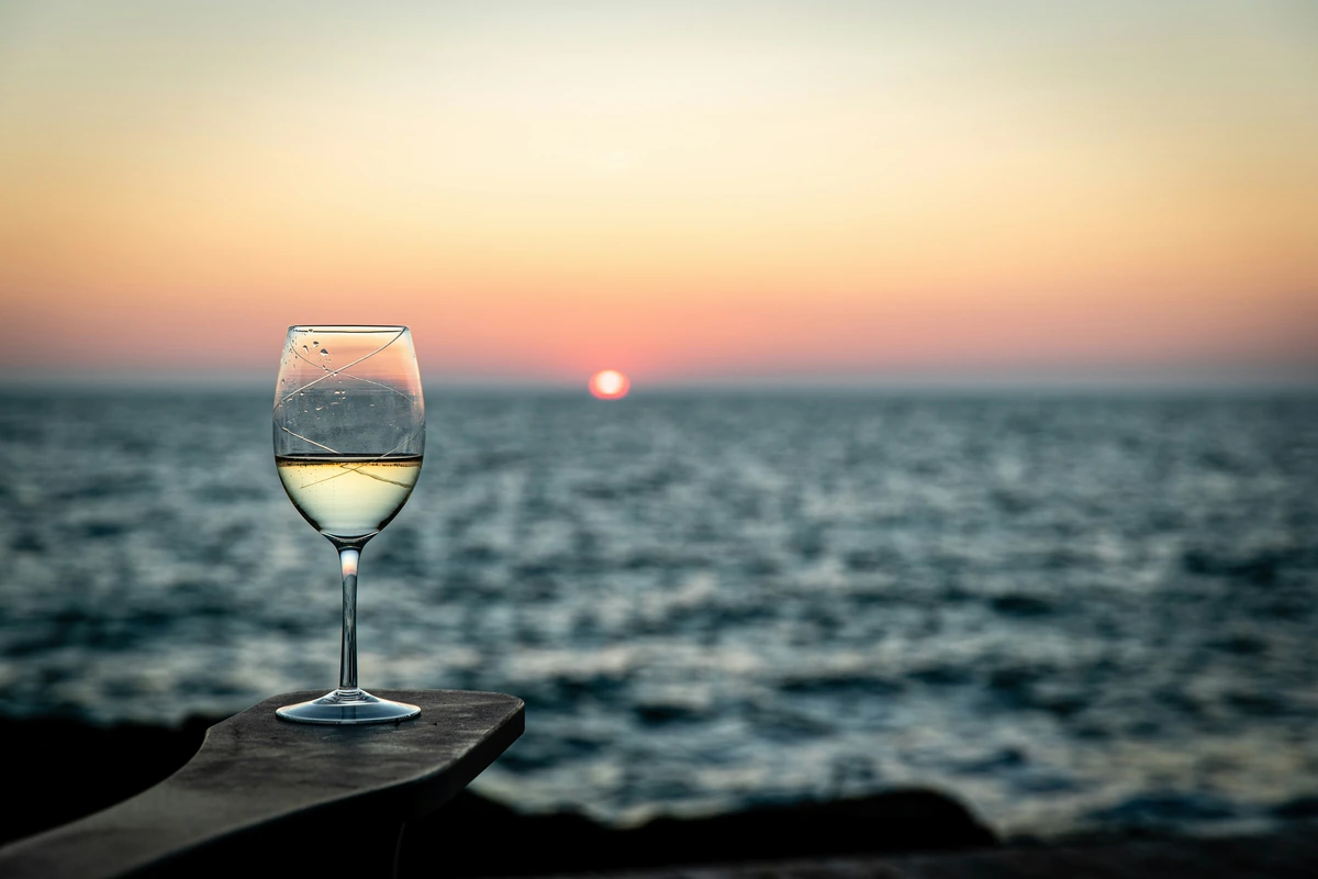 Taça de vinho branco junto ao mar ao pôr do sol.