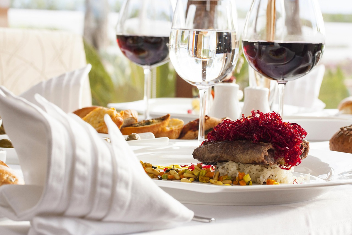 Prato de carne com arroz e legumes, acompanhado de taças de vinho tinto.