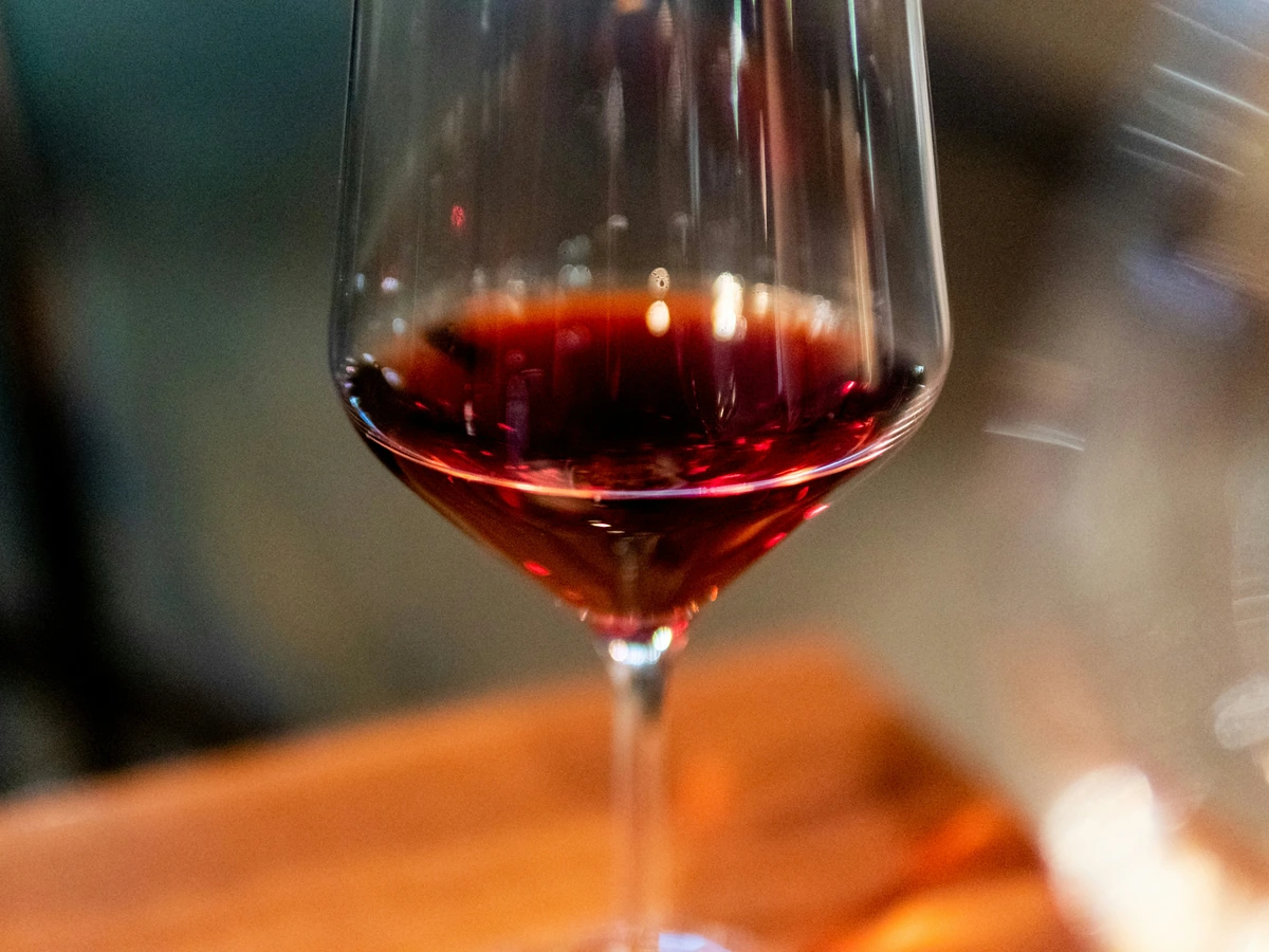 Detalhe de vinho tinto rubi em taça, com madeira e iluminação quente.