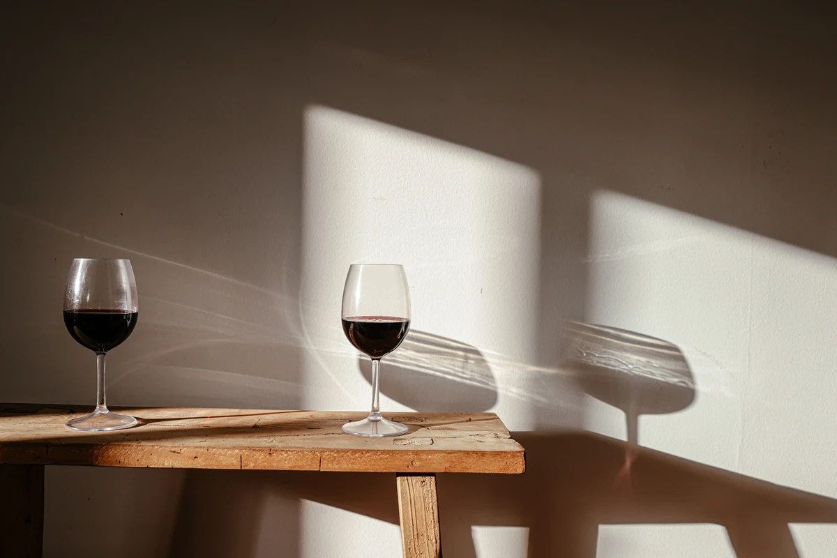 Duas taças de vinho tinto sobre mesa de madeira, iluminadas lateralmente.