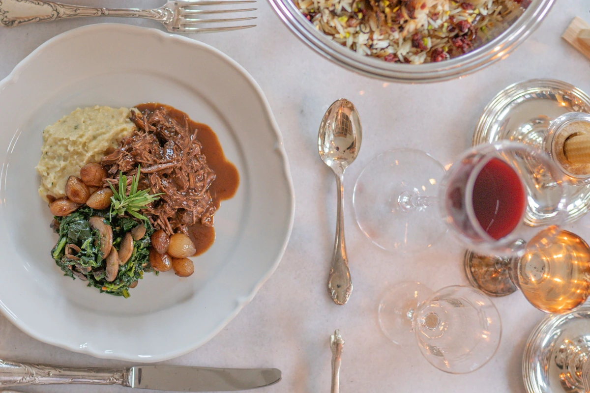 Carne em molho com cogumelos e acompanhamento cremoso ao lado de uma taça de vinho tinto