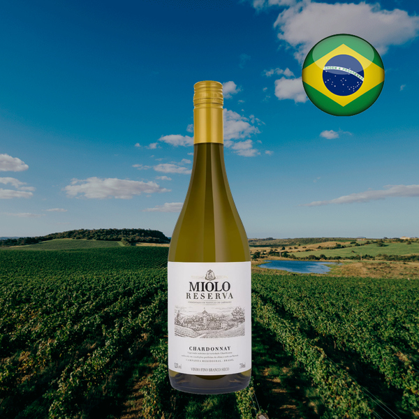 Imagem quadrada de Miolo Reserva Chardonnay, com cápsula dourada e rótulo branco, diante de fileiras de videiras, um lago e céu azul, com bandeira do Brasil.