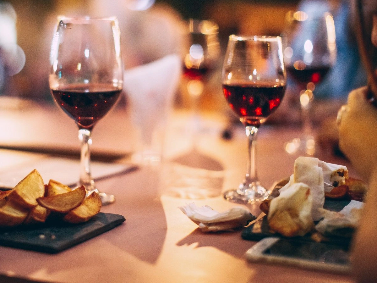 Duas taças preenchidas com vinho tinto rubi sobre mesa de jantar com petiscos, sob luz quente.