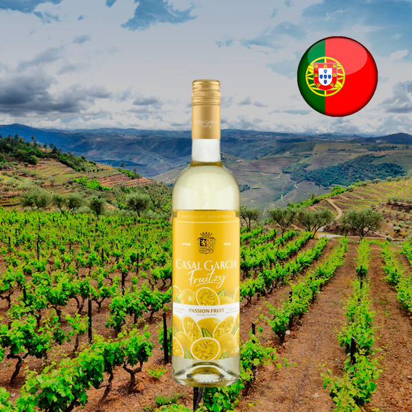 Garrafa de Casal Garcia Fruitzy Maracujá, com fechamento dourado e rótulo amarelo ilustrado com maracujás, diante de vinhedos em encostas sob céu nublado, com bandeira portuguesa.