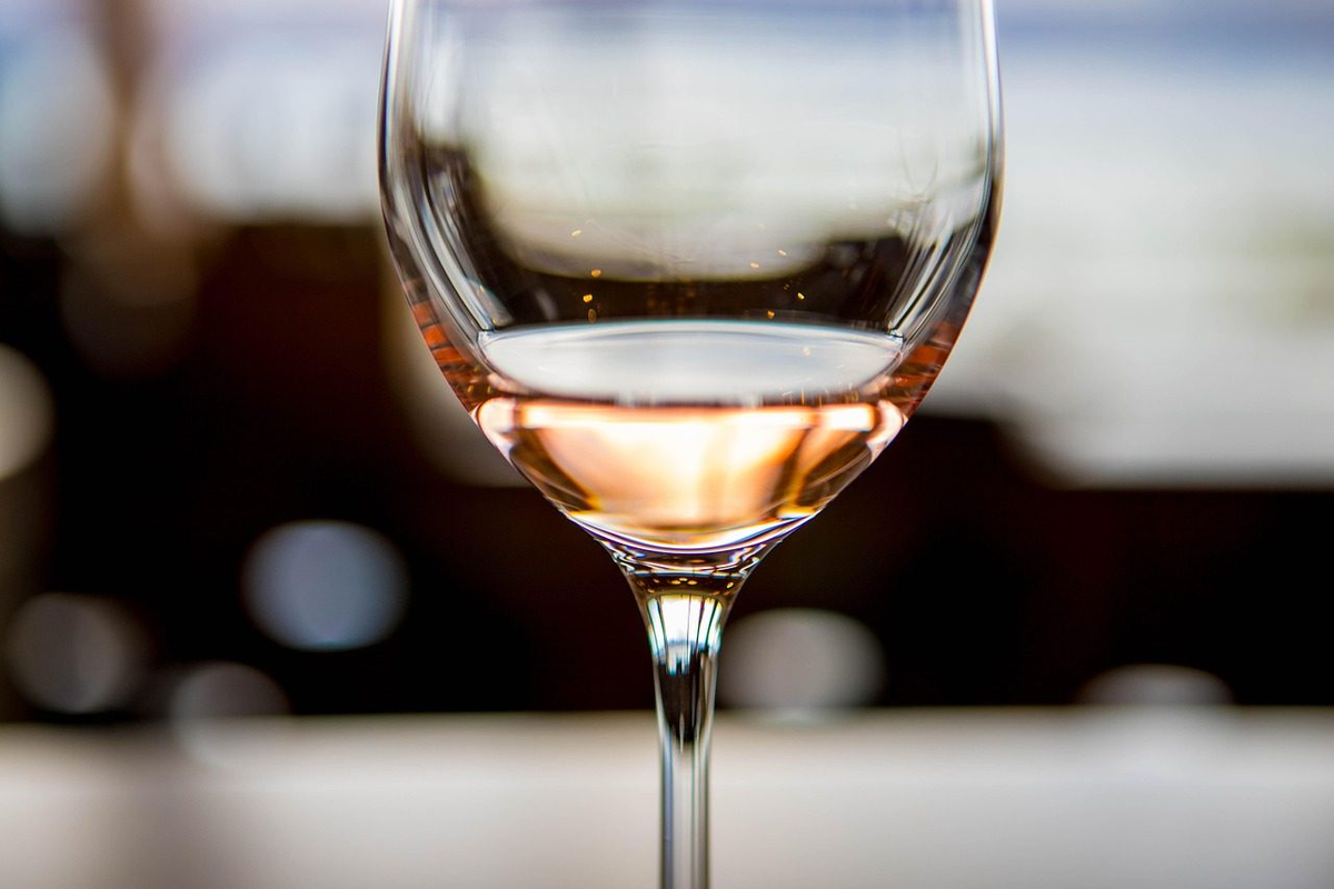 Detalhe de taça parcialmente preenchida com vinho rosé salmão claro sobre mesa clara, com fundo desfocado.