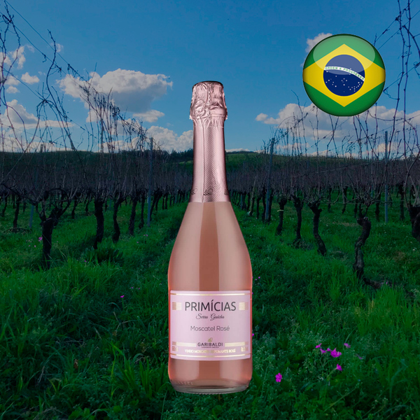 Garrafa rosada do Garibaldi Primícias Moscatel Rosé 660 ml, com cápsula rosa e rótulo claro, diante de parreiras sem folhas, gramado verde com flores rosas e céu azul; bandeira brasileira no alto à direita.