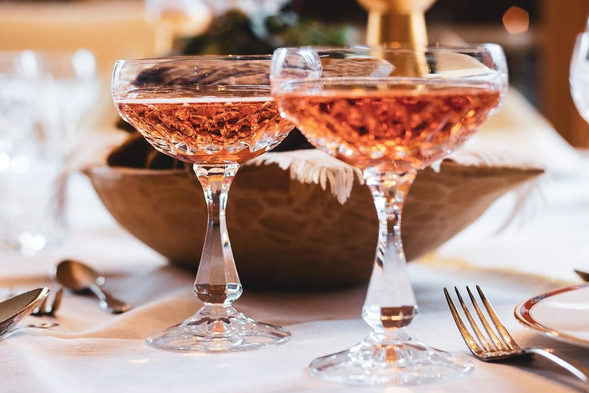 Duas taças coupe preenchidas com espumante rosado-salmão sobre mesa posta com toalha branca.