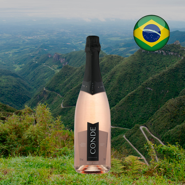 Garrafa do Conde de Foucauld Brut Rosé 750 ml, com cápsula preta e vinho rosado, diante de vale montanhoso verde e estrada sinuosa, em enquadramento quadrado com bandeira brasileira no alto à direita.
