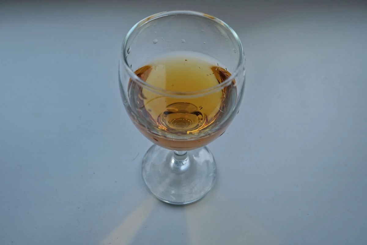 Taça preenchida de vinho âmbar dourado sobre superfície clara, vista em diagonal.