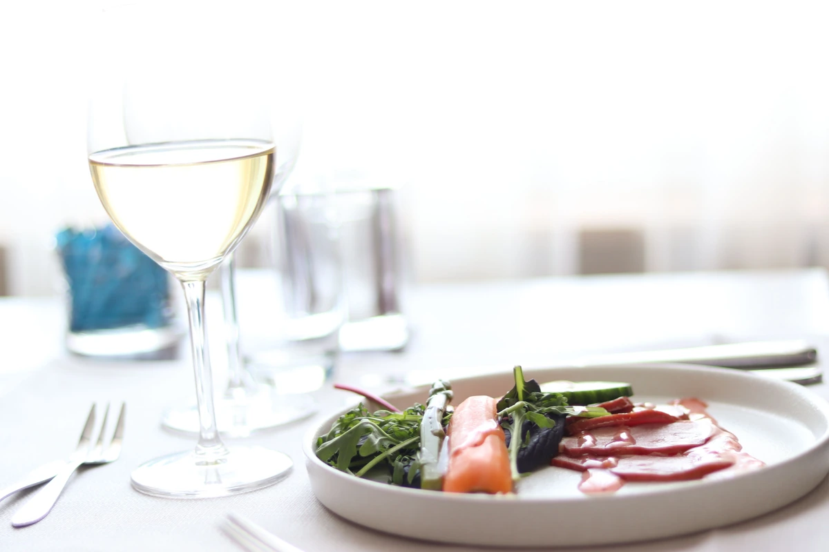 Salada com folhas e fatias de beterraba ao lado de taça preenchida de vinho branco.