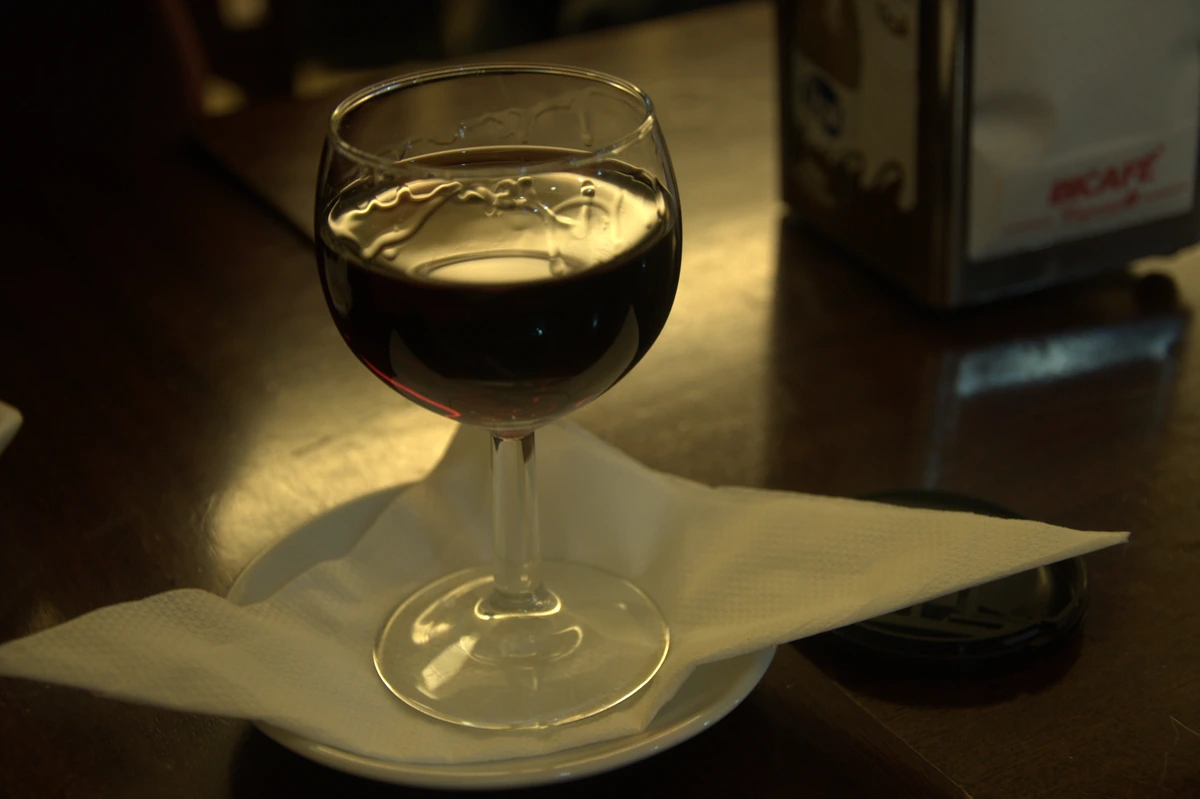 Taça de vinho do Porto sobre pires e guardanapo em balcão de madeira.