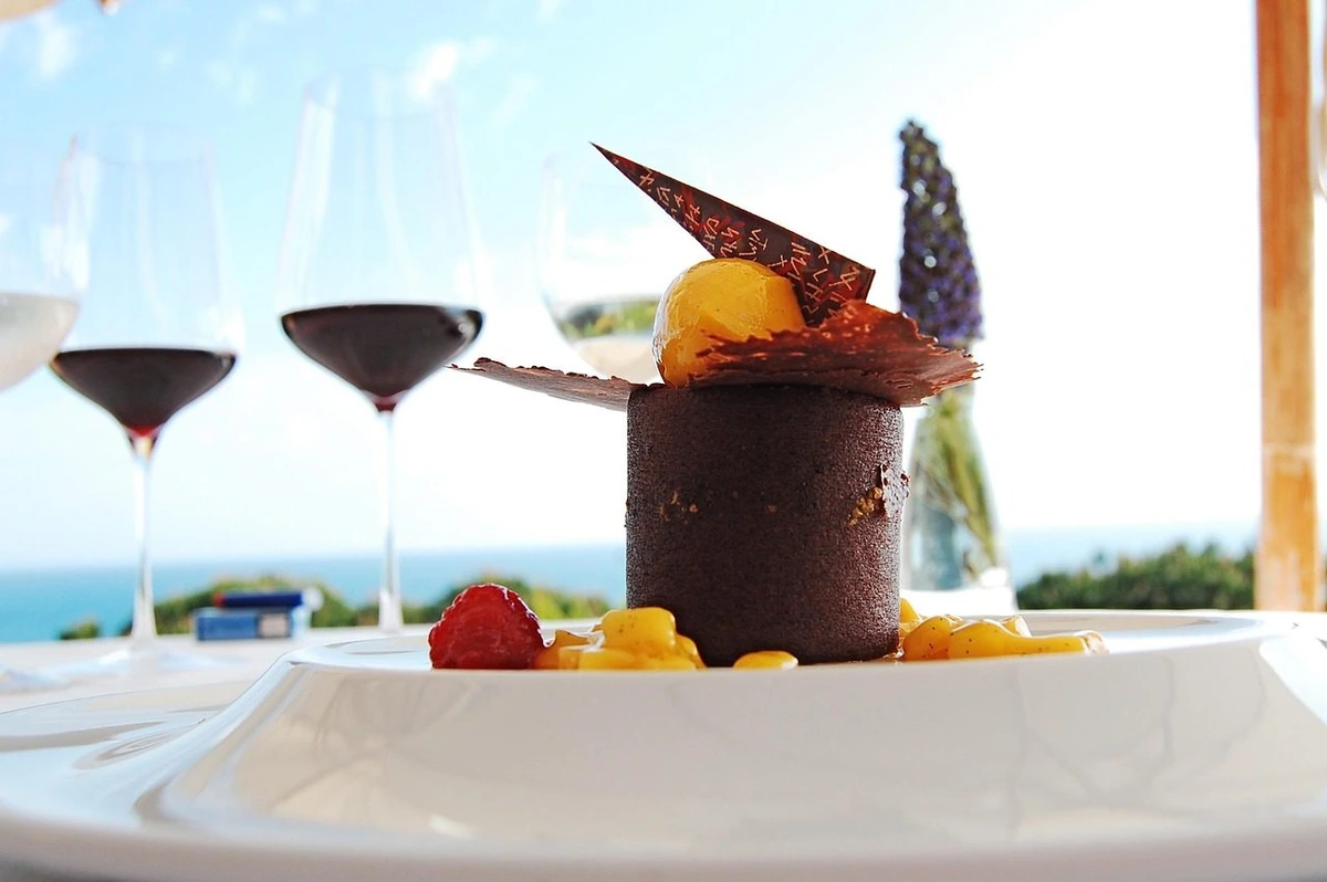 Sobremesa de chocolate com frutas vermelhas e taças de vinho sobre a mesa.