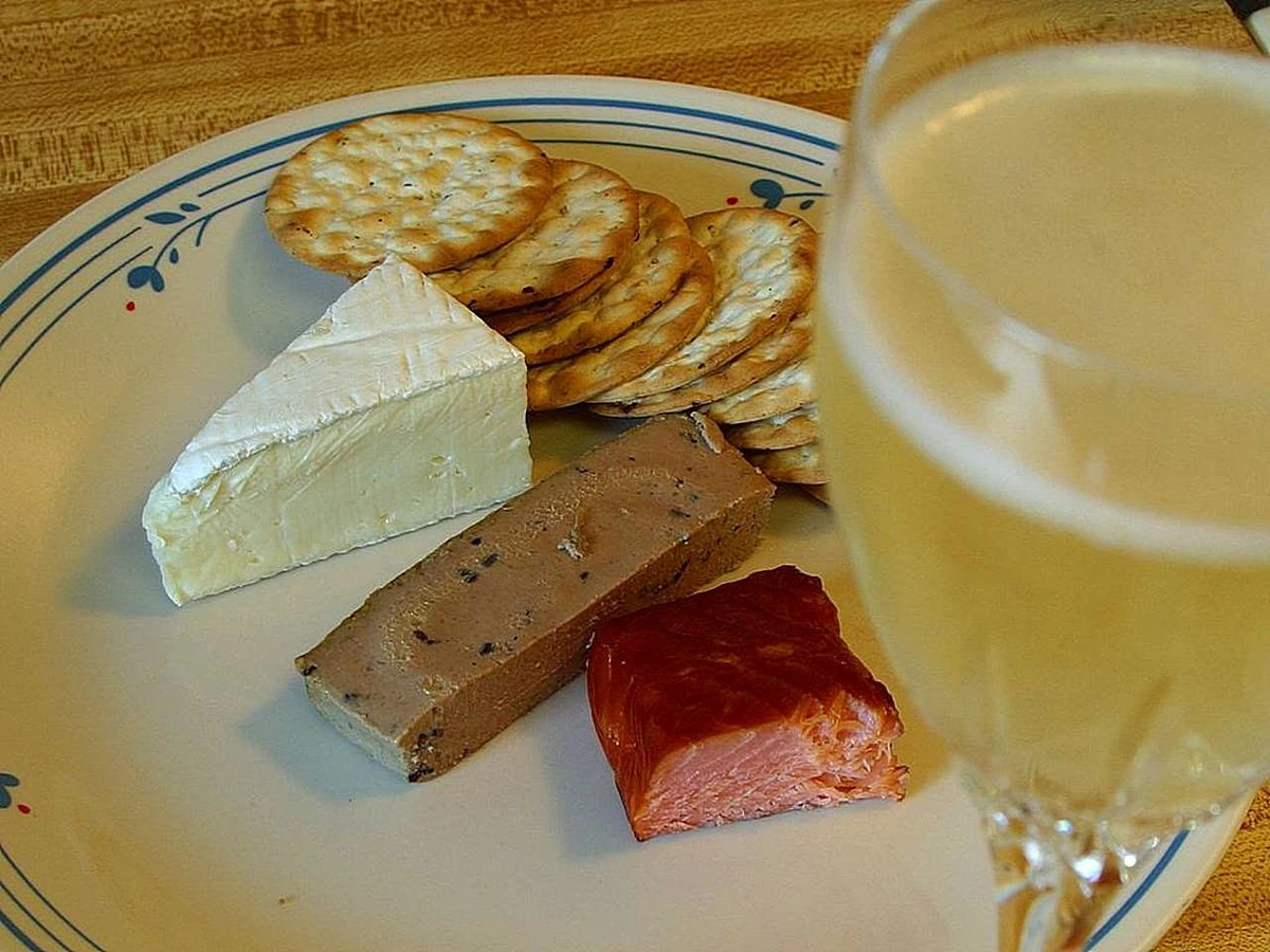 Queijo brie, patê e crackers ao lado de uma taça preenchida de espumante branco.