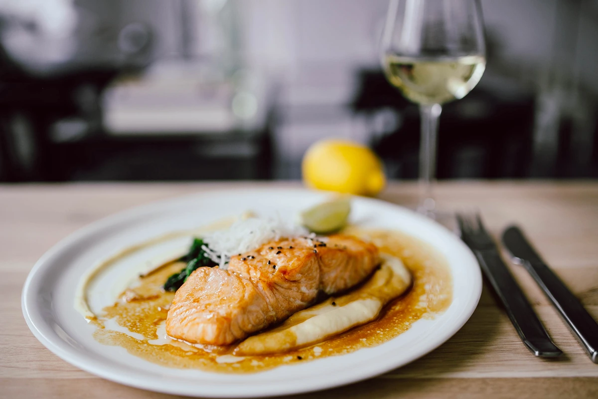 Filé de salmão com purê e molho, acompanhado de taça preenchida de vinho branco.