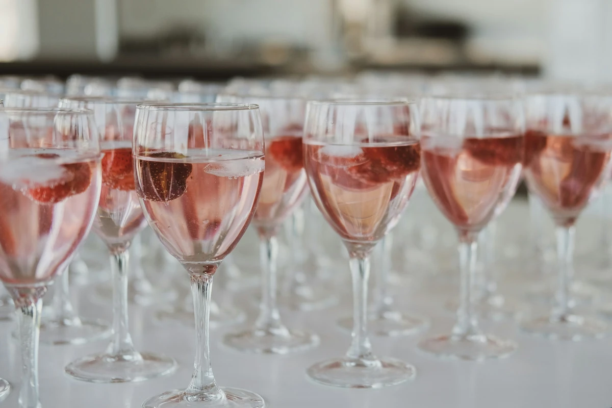 Taças alinhadas com espumante rosé, pequenas bolhas e espuma fina sobre mesa branca.