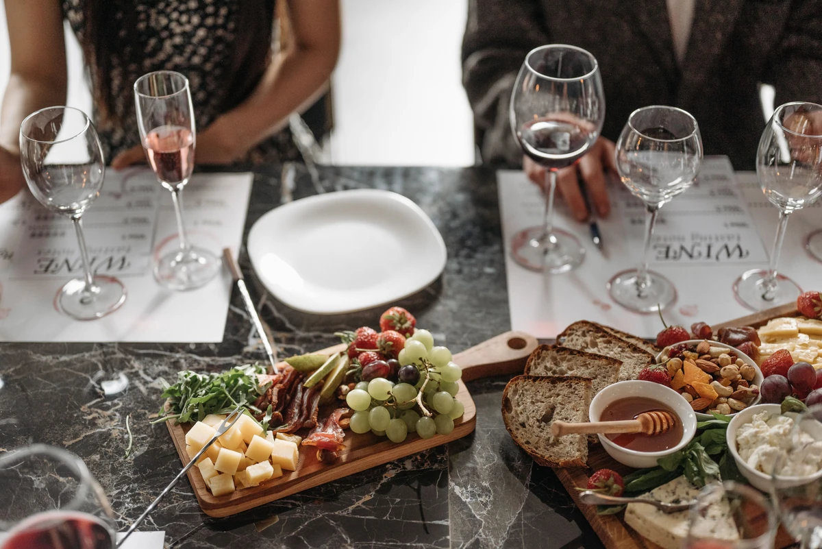 Tábuas de queijos, pães e frutas junto a uma flute de espumante rosé em mesa compartilhada.