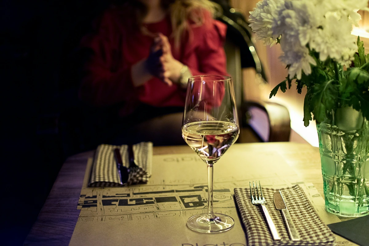 Taça de vinho branco em mesa de restaurante, com flores claras ao lado.
