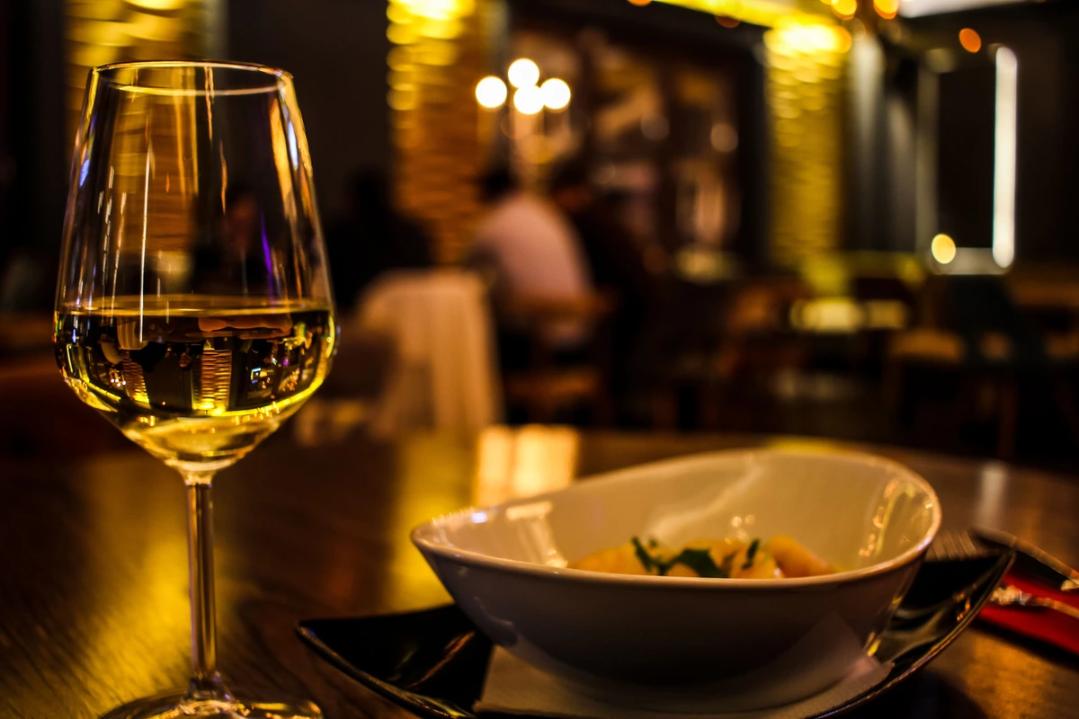 Massa curta com folhas verdes e taça preenchida de vinho branco à mesa.