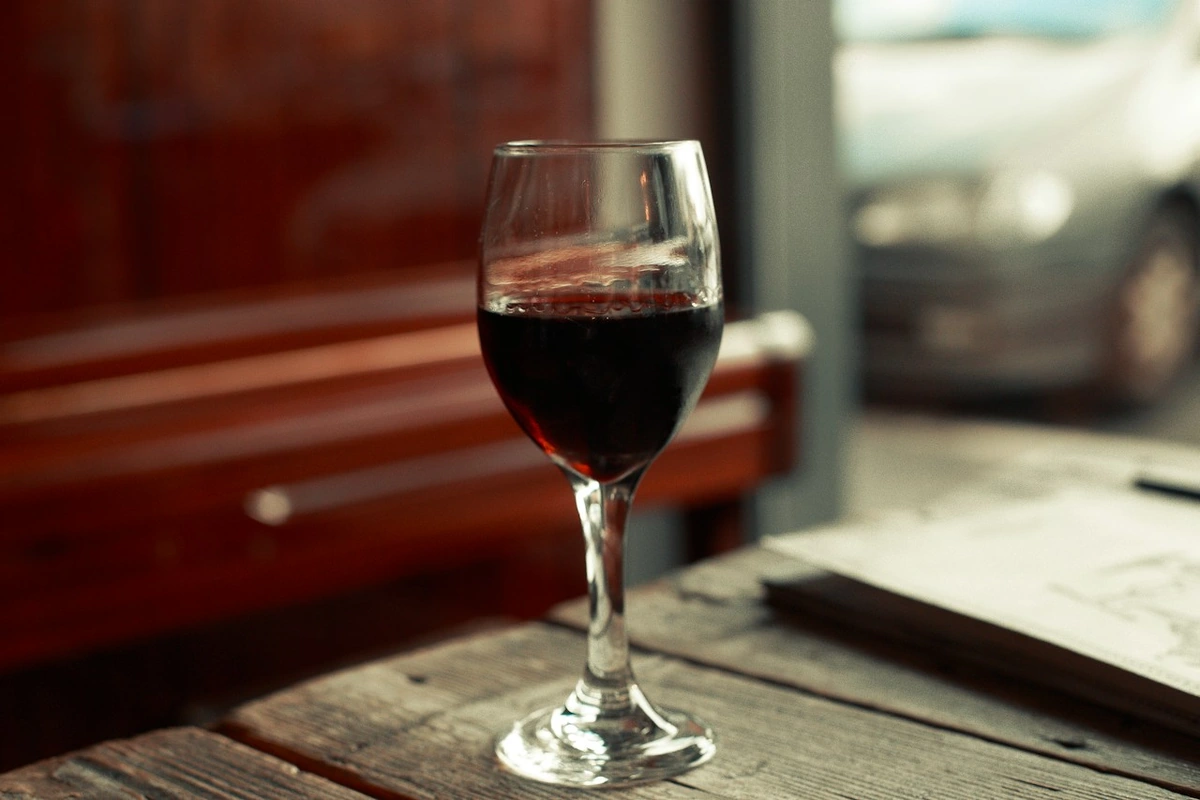 Taça de vinho tinto sobre mesa de madeira, com cardápio ao lado.